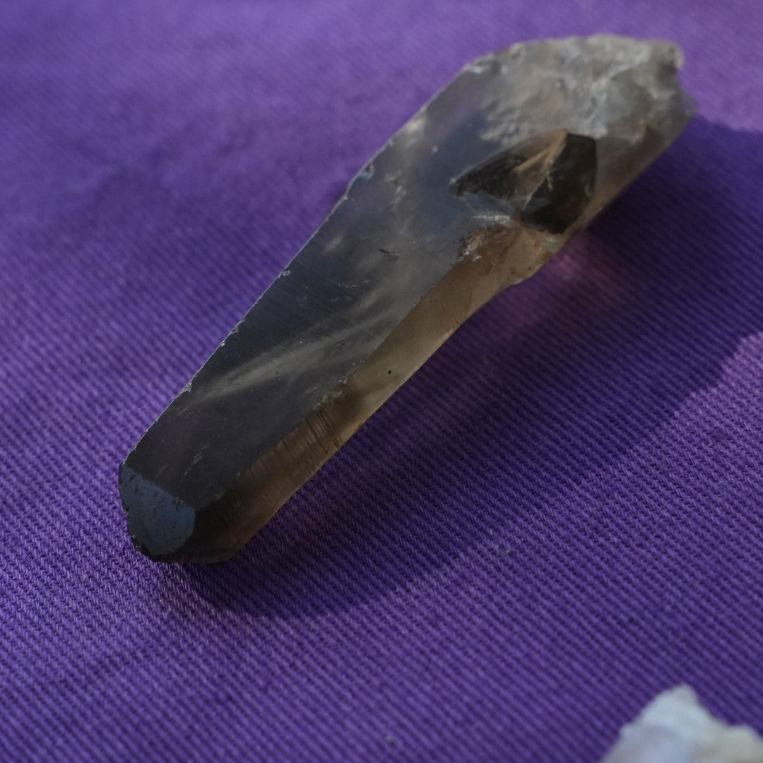 A single smokey quartz point on purple cloth