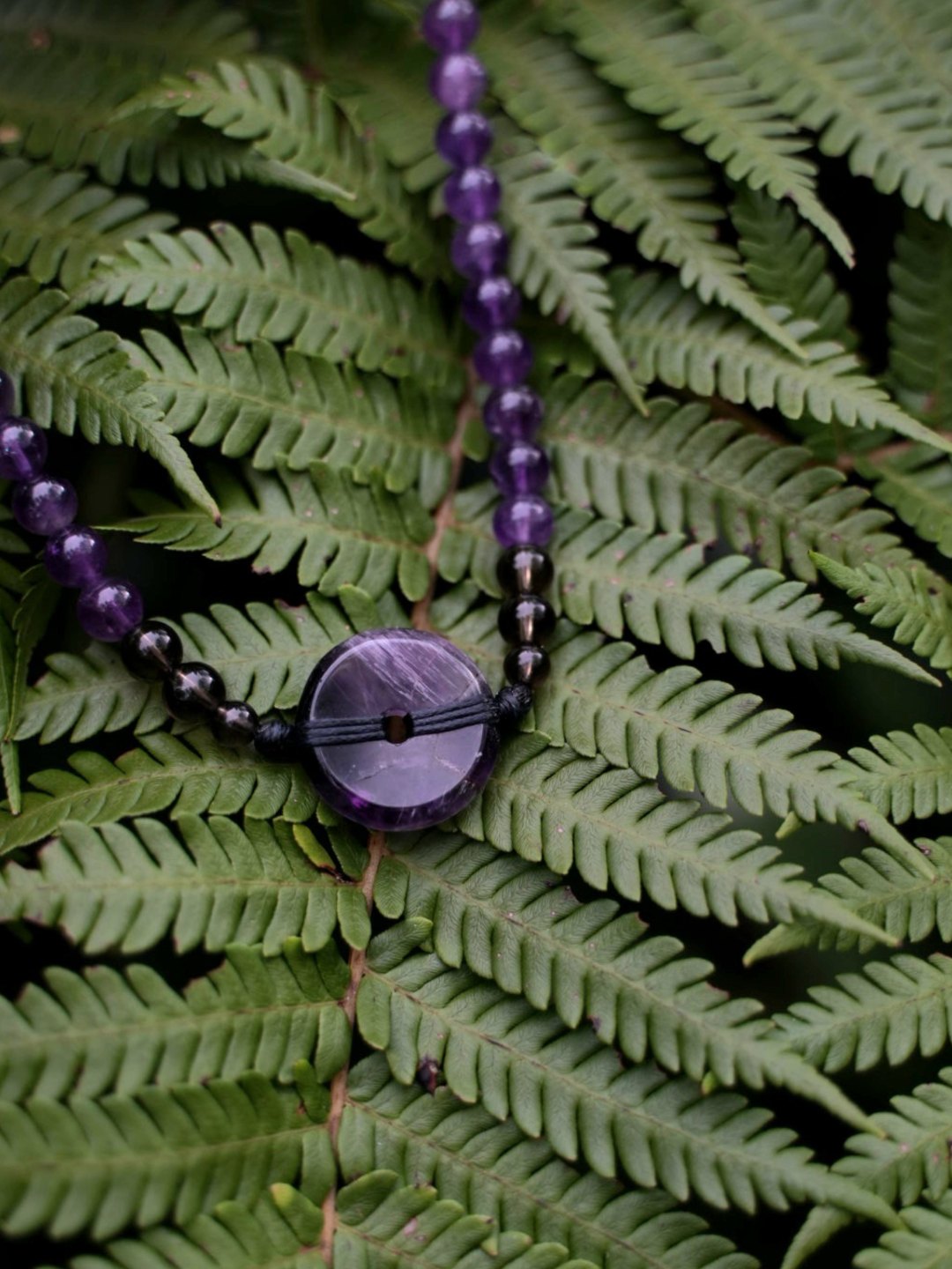 An amethyst bead necklace resting on a fern