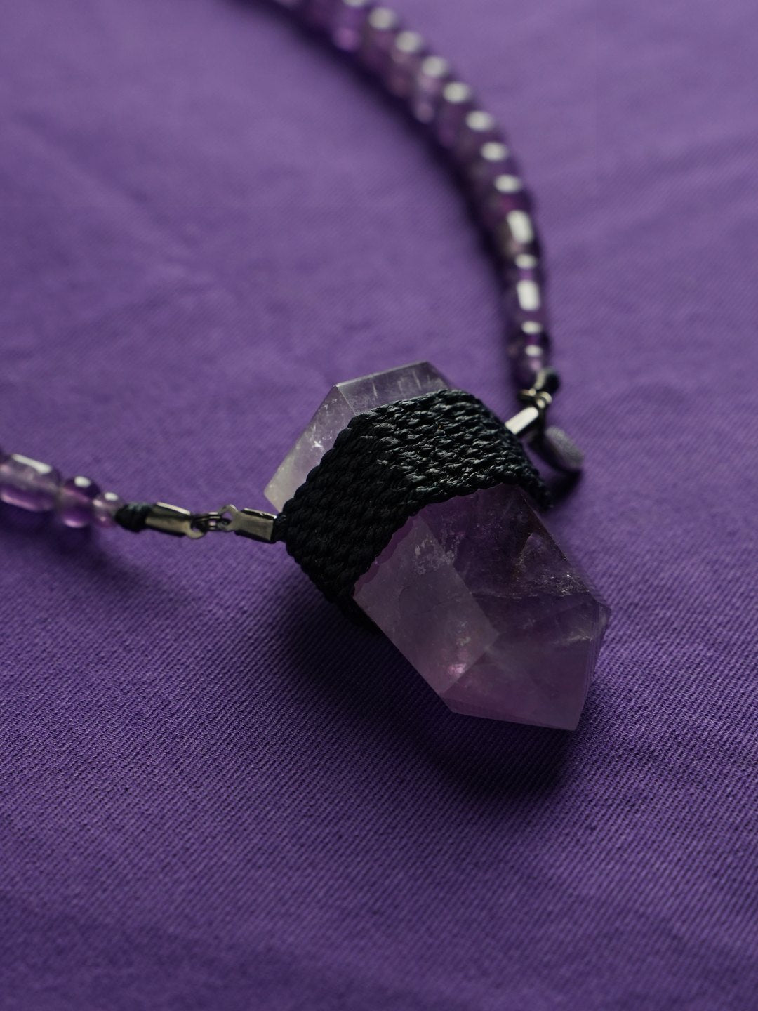 A cord-wrapped amethyst point on purple cloth