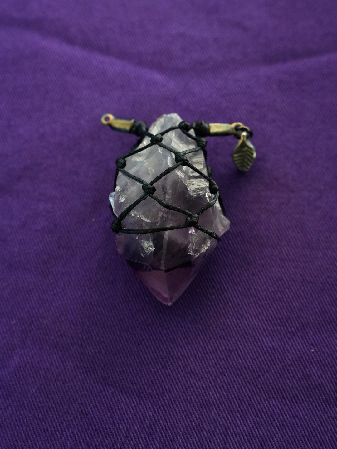 A rough amethyst netted in black cord on purple cloth