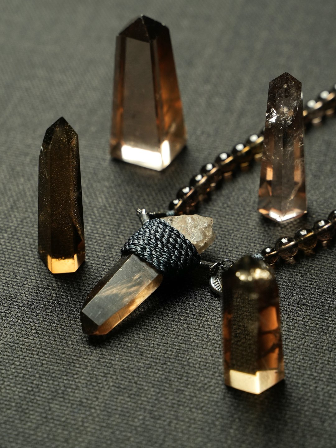 Smokey quartz points glowing on charcoal cloth around a wrapped smokey quartz pendant