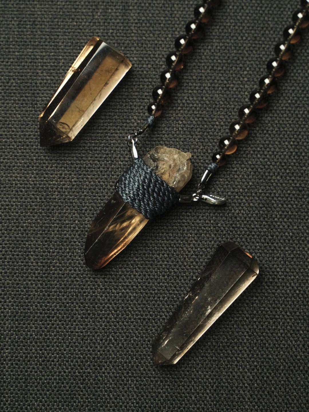 A cord-wrapped smokey quartz pendant among smokey points on charcoal cloth