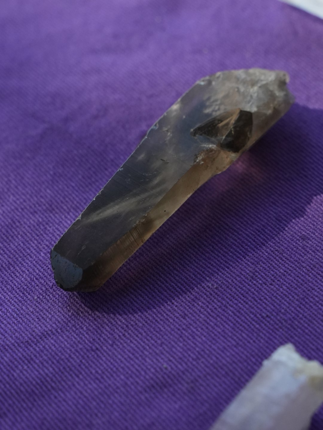 A long smokey quartz point on purple cloth