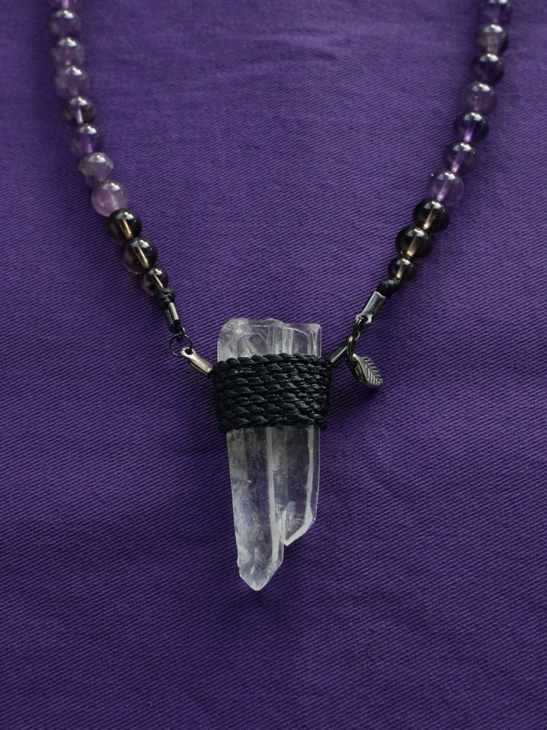 A cord-wrapped clear quartz necklace on purple cloth