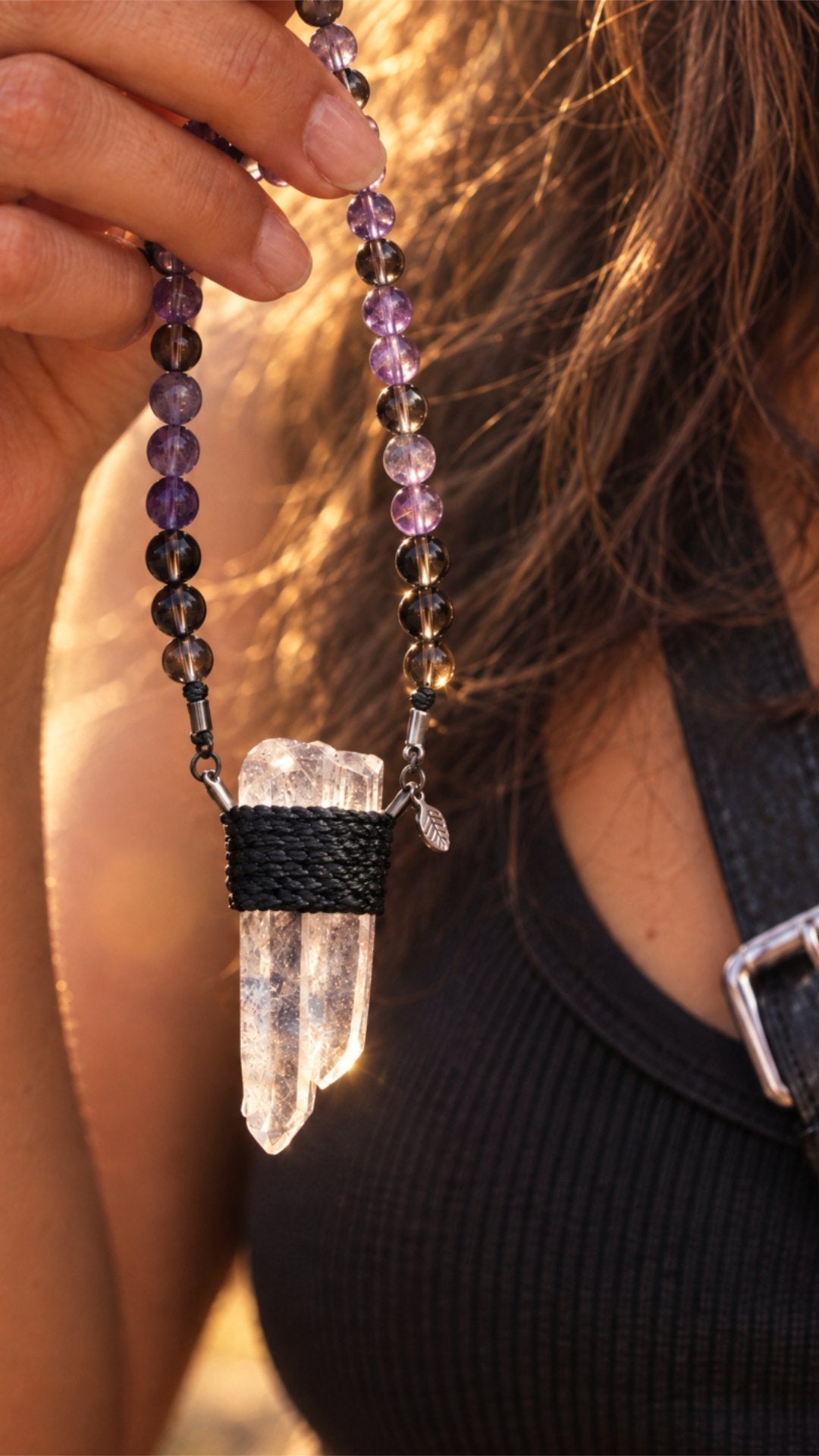 A hand holding a Clink clear quartz pendant against long hair