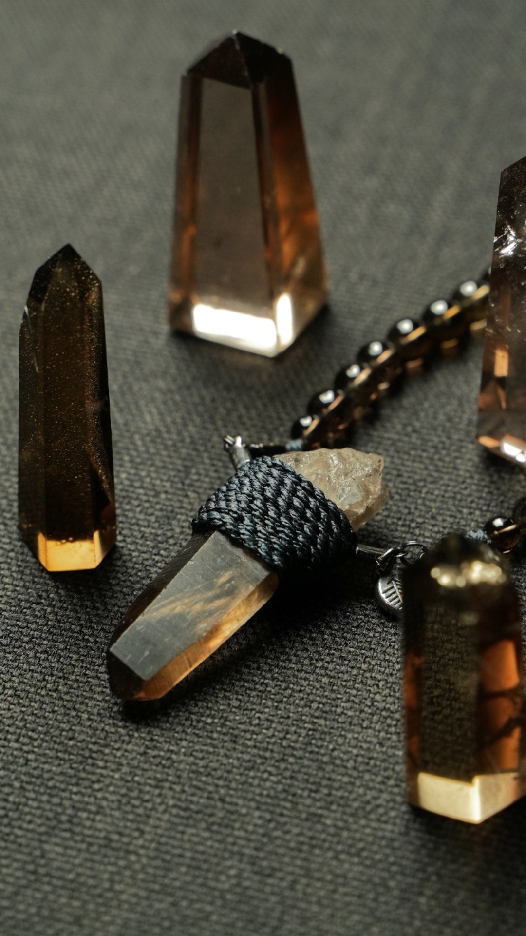 Smokey quartz points glowing on charcoal cloth around a wrapped smokey quartz pendant