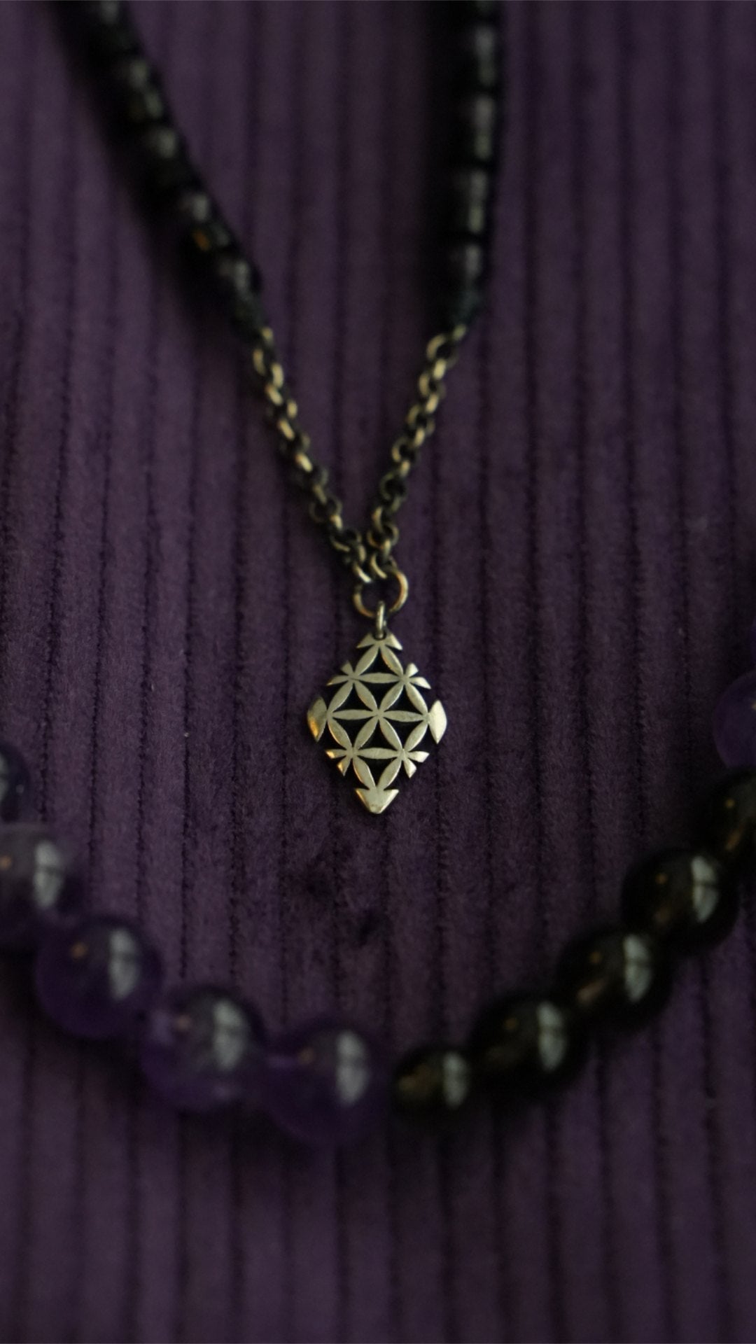 A Clink silver pendant on a bead necklace over purple corduroy