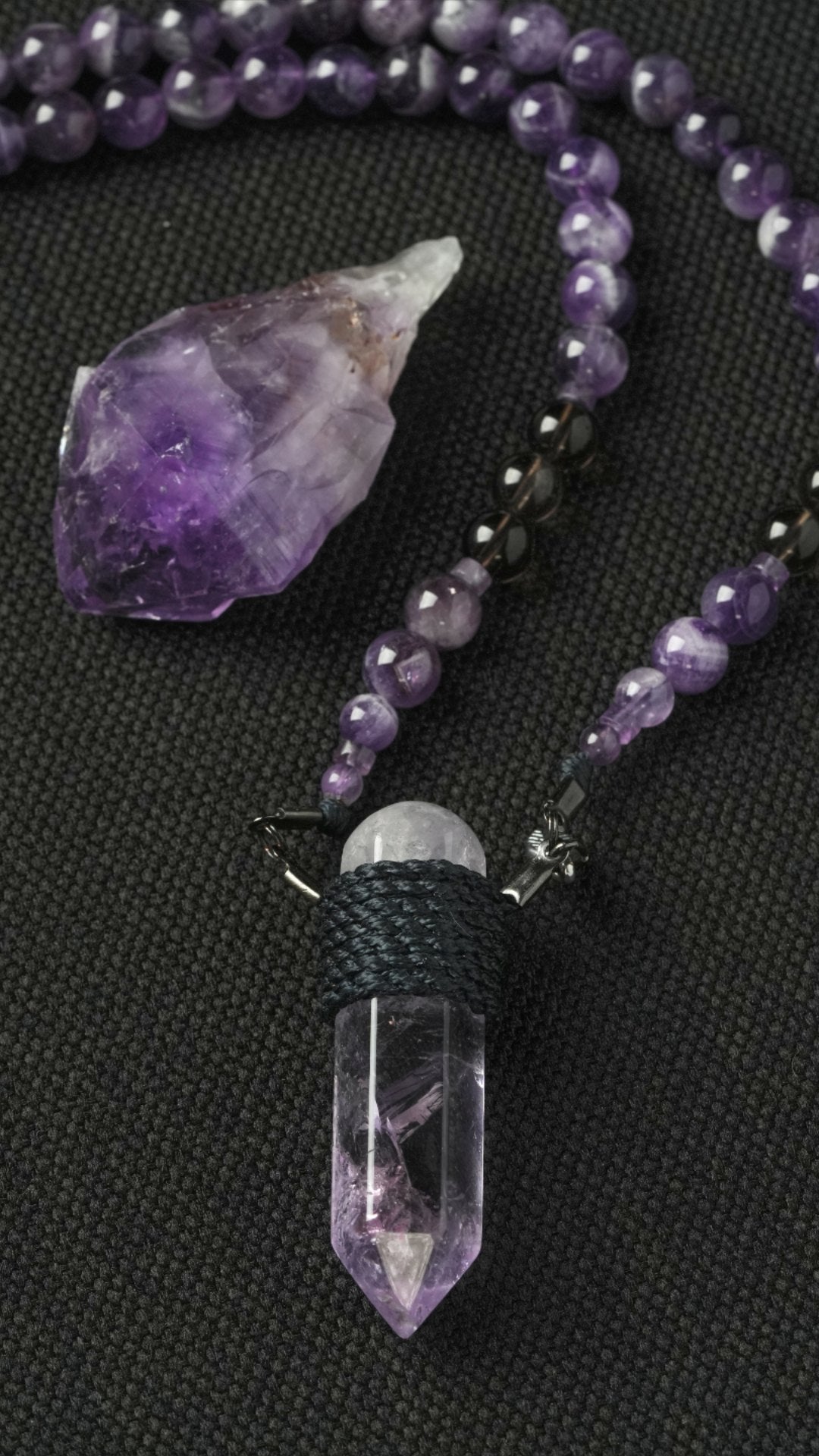 A rough amethyst and a wrapped clear quartz pendant on charcoal cloth